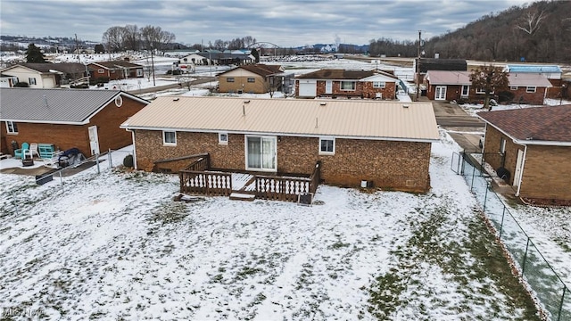 snow covered house with metal roof, a wooden deck, a residential view, and fence