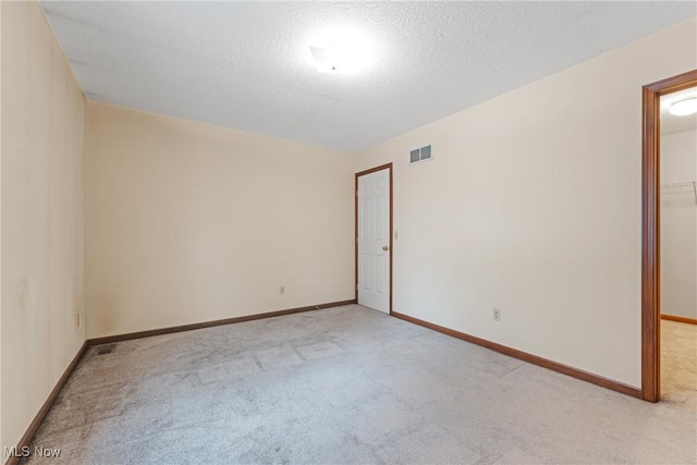 spare room with light carpet, a textured ceiling, visible vents, and baseboards