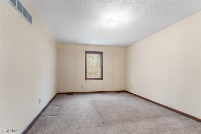 spare room with light carpet, a textured ceiling, visible vents, and baseboards