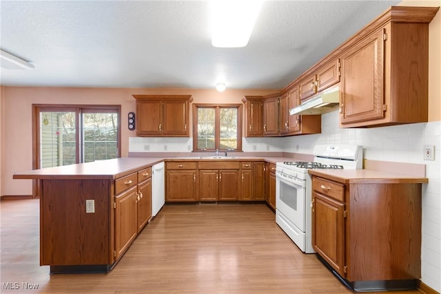 kitchen featuring a peninsula, white appliances, light countertops, and under cabinet range hood