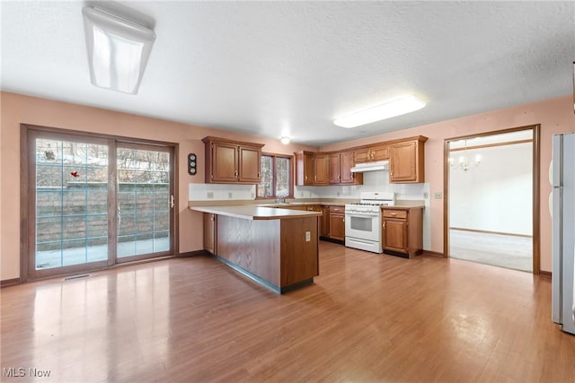 kitchen with white gas range, light countertops, brown cabinetry, a peninsula, and under cabinet range hood