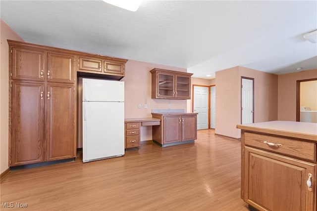 kitchen with brown cabinetry, glass insert cabinets, and freestanding refrigerator