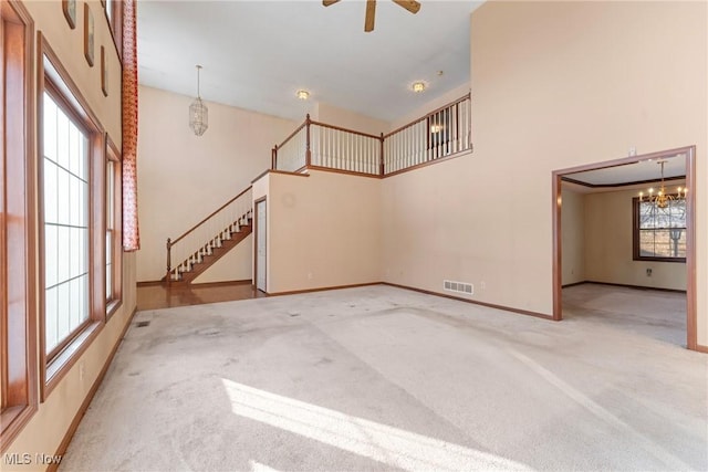 unfurnished living room featuring carpet floors, visible vents, a towering ceiling, baseboards, and stairs