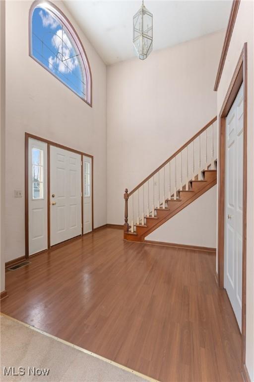 foyer featuring baseboards, wood finished floors, stairs, a high ceiling, and a chandelier