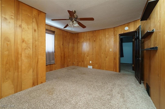 empty room featuring carpet, visible vents, a ceiling fan, wood walls, and a textured ceiling