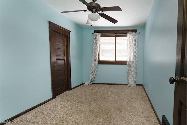 spare room featuring light carpet, ceiling fan, and baseboards