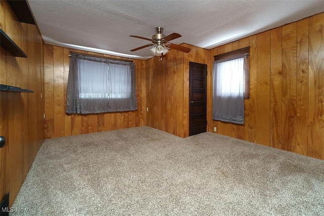 carpeted empty room with wooden walls, a ceiling fan, and a textured ceiling