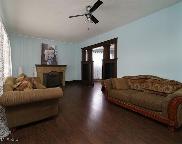 living area with dark wood-type flooring, a fireplace, and a ceiling fan