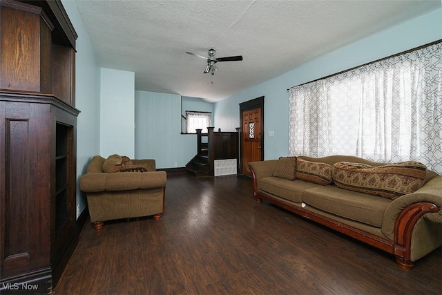 living area featuring stairway, dark wood-style flooring, ceiling fan, and a textured ceiling