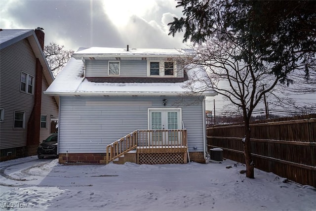 snow covered back of property with french doors, fence, and central AC unit