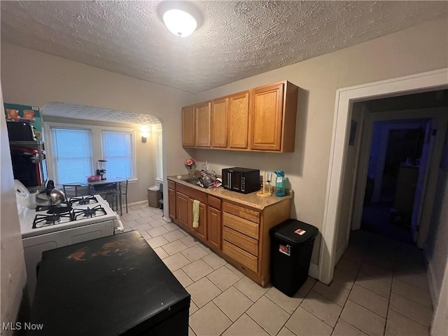 kitchen featuring light countertops, white gas stove, a textured ceiling, and light tile patterned flooring