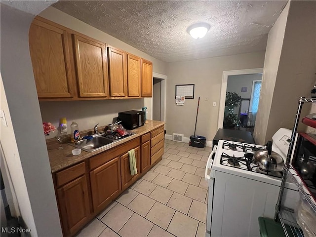 kitchen with light tile patterned flooring, a sink, a textured ceiling, black microwave, and white gas range oven