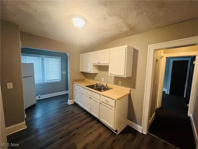 kitchen with white cabinets, dark wood-type flooring, freestanding refrigerator, light countertops, and a sink