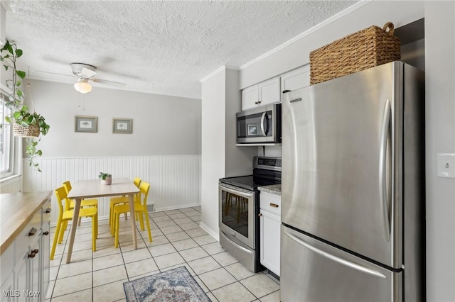 kitchen featuring light tile patterned flooring, white cabinets, light countertops, appliances with stainless steel finishes, and wainscoting