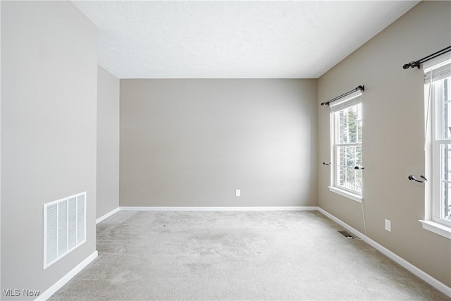 unfurnished room featuring light carpet, a textured ceiling, visible vents, and baseboards