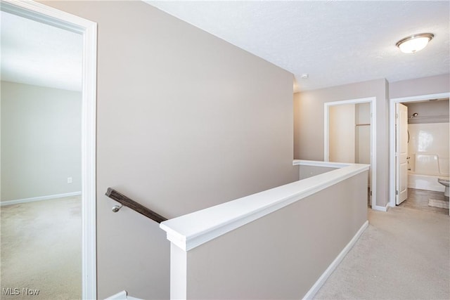 hallway with baseboards, an upstairs landing, and light colored carpet