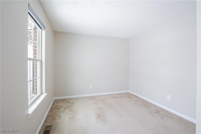 spare room featuring light carpet, visible vents, and baseboards