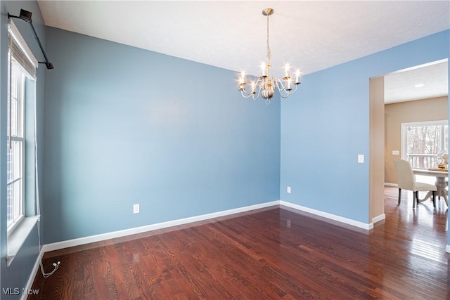 spare room with baseboards, a chandelier, and dark wood-type flooring