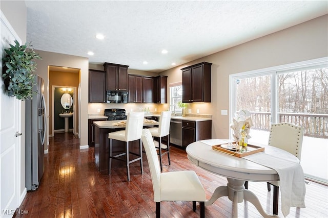 kitchen featuring dark wood-style flooring, a kitchen island, dark brown cabinets, black appliances, and a kitchen bar