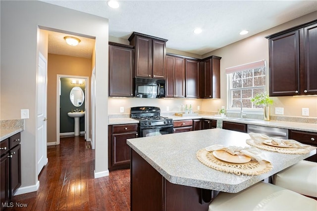 kitchen with black appliances, a kitchen bar, light countertops, and dark wood-type flooring