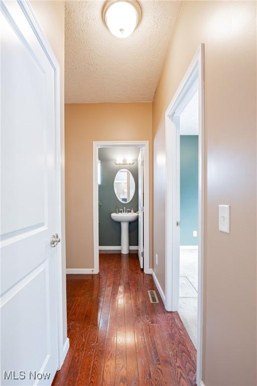 hall with dark wood-style flooring, visible vents, a sink, a textured ceiling, and baseboards