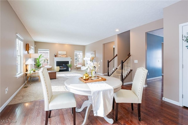 dining room with dark wood-style floors, a glass covered fireplace, stairs, and baseboards