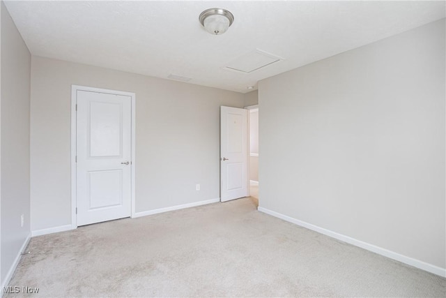 empty room featuring attic access, baseboards, and light colored carpet