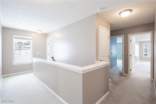 hallway with light carpet, baseboards, a textured ceiling, and an upstairs landing