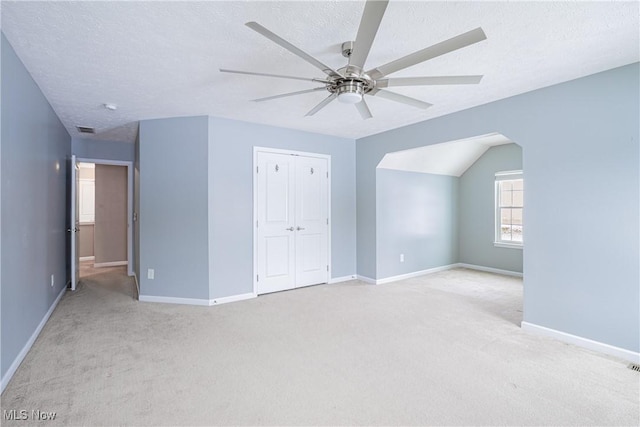 unfurnished bedroom featuring a closet, light carpet, a textured ceiling, and baseboards