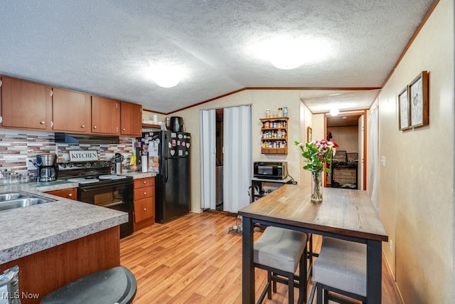 kitchen with brown cabinets, light wood finished floors, lofted ceiling, light countertops, and black appliances