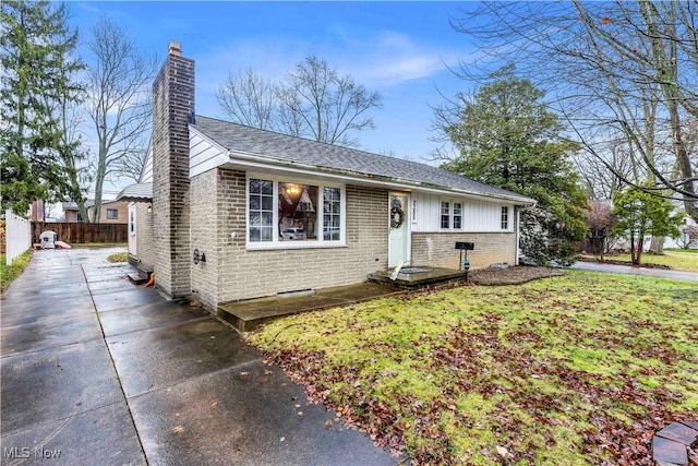 view of front of house featuring brick siding, fence, concrete driveway, a front lawn, and a chimney