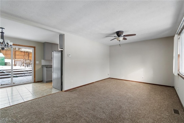 spare room featuring visible vents, light carpet, a textured ceiling, baseboards, and ceiling fan with notable chandelier