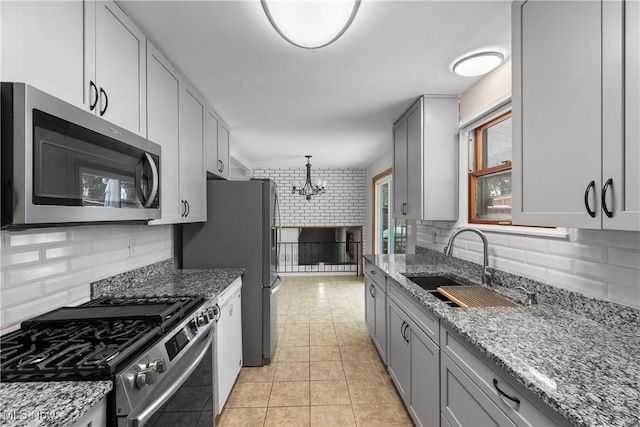 kitchen with light stone counters, a sink, stainless steel appliances, a notable chandelier, and light tile patterned flooring