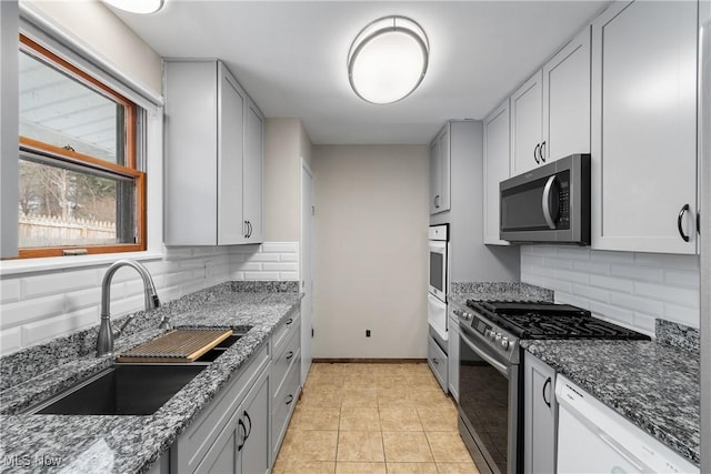 kitchen with appliances with stainless steel finishes, dark stone counters, light tile patterned flooring, and a sink