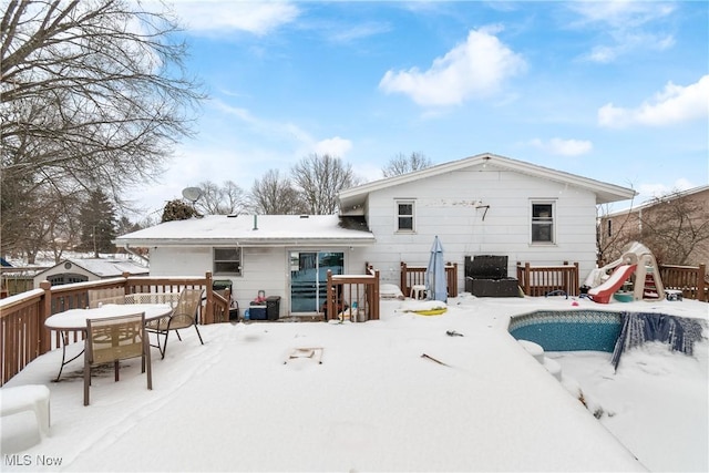 snow covered rear of property featuring a playground and a deck