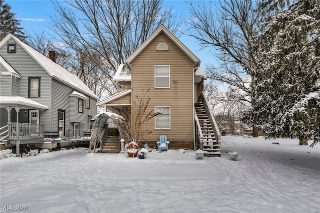 snow covered rear of property featuring stairs