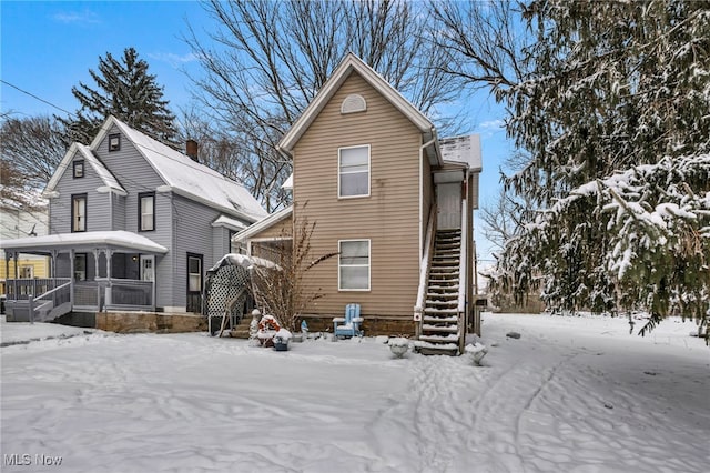 snow covered house with covered porch and stairway