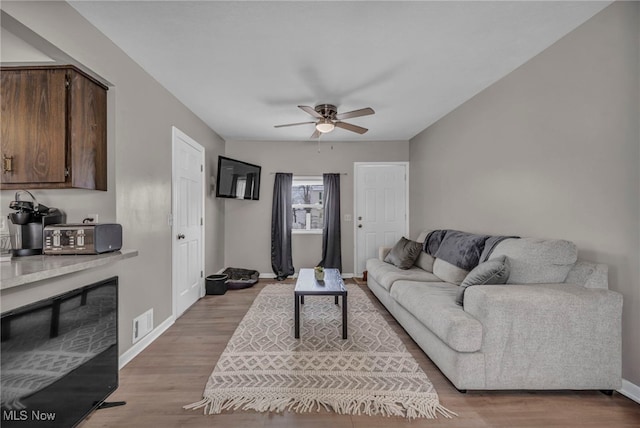 living area featuring baseboards, a ceiling fan, visible vents, and light wood-style floors