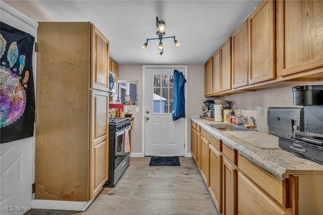 kitchen with a sink, baseboards, light wood-style floors, appliances with stainless steel finishes, and light stone countertops