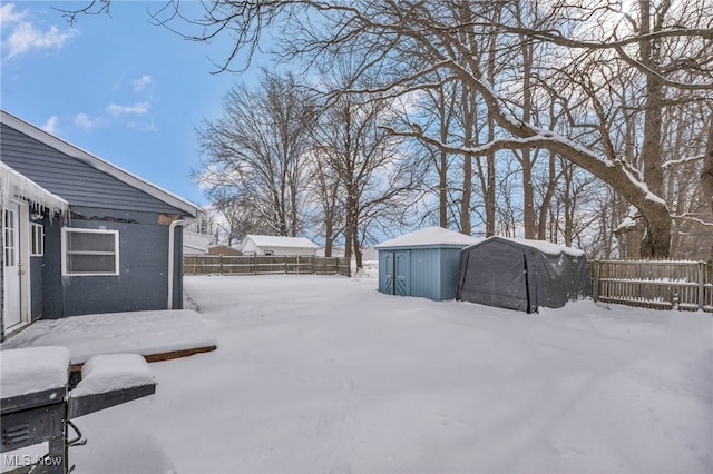 yard layered in snow with a storage shed, fence, and an outdoor structure