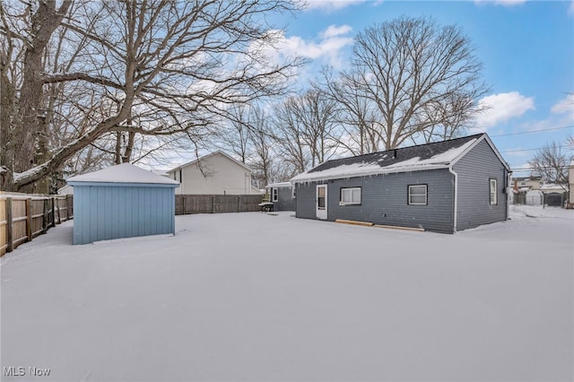 snow covered rear of property with a storage unit, an outdoor structure, and fence