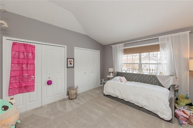 carpeted bedroom with vaulted ceiling and two closets