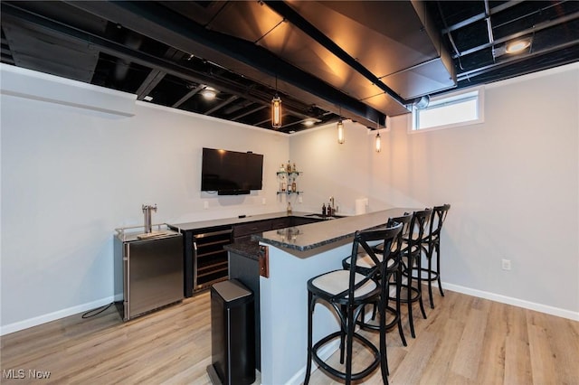 bar with light wood-type flooring, indoor wet bar, a sink, and baseboards