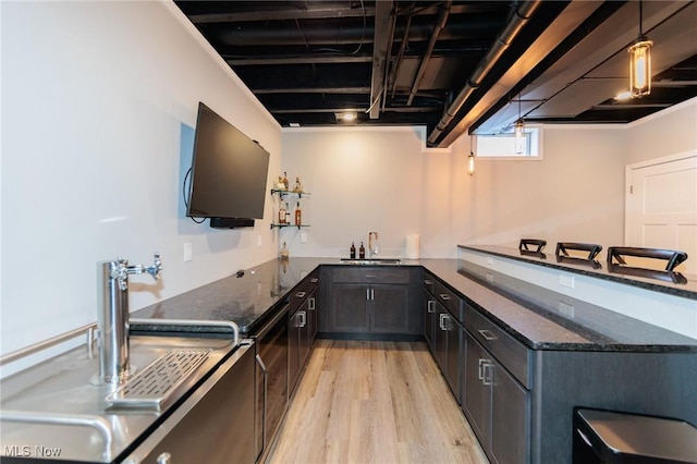 kitchen with light wood-style flooring, a sink, a kitchen breakfast bar, dark stone counters, and pendant lighting