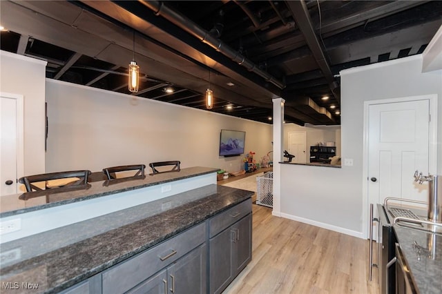 kitchen featuring hanging light fixtures, light wood-type flooring, baseboards, and dark stone countertops