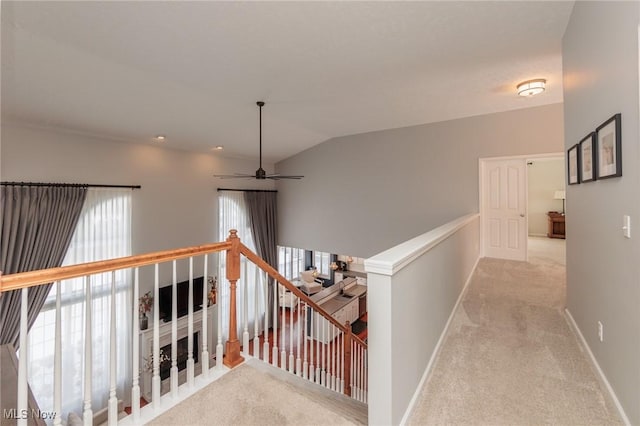 hall with lofted ceiling, baseboards, light carpet, and an upstairs landing