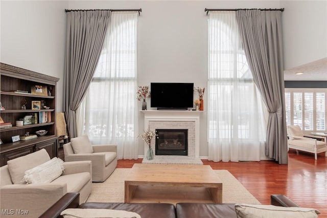 living area featuring a towering ceiling, a glass covered fireplace, and light wood-style flooring