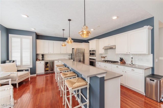 kitchen featuring pendant lighting, appliances with stainless steel finishes, white cabinetry, beverage cooler, and under cabinet range hood