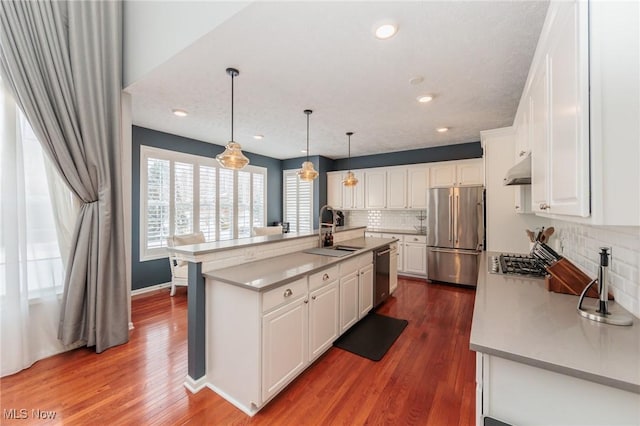 kitchen featuring white cabinets, appliances with stainless steel finishes, under cabinet range hood, pendant lighting, and a sink