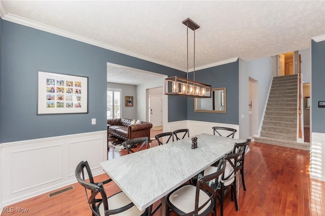 dining space with visible vents, wainscoting, a textured ceiling, wood finished floors, and stairs